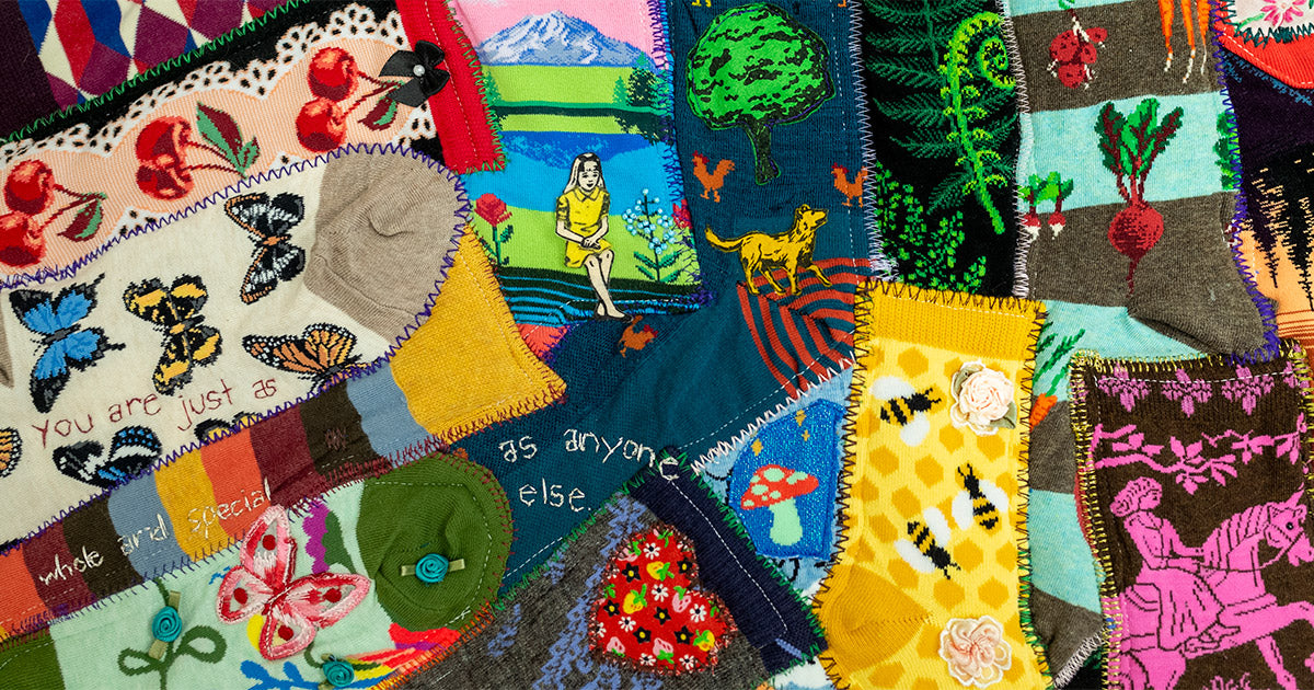 A Victorian crazy quilt made from socks and vintage fabric scraps, embroidered with messages promoting mental health awareness.