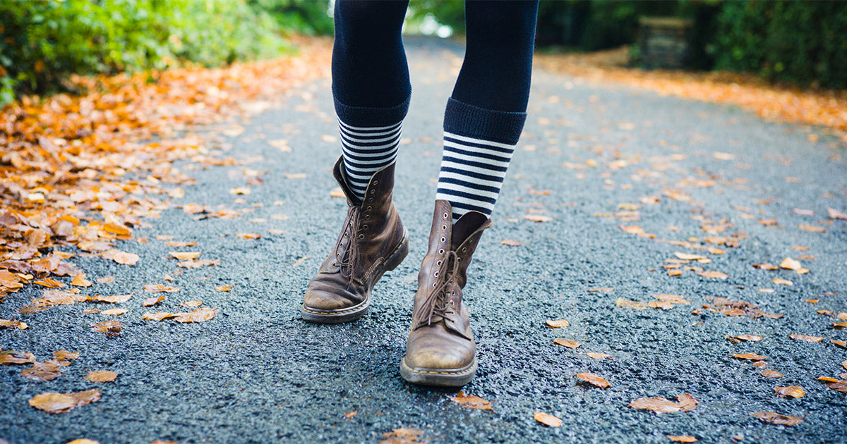 Charcoal gray and white striped socks worn with brown combat boots by a model walking in a park.