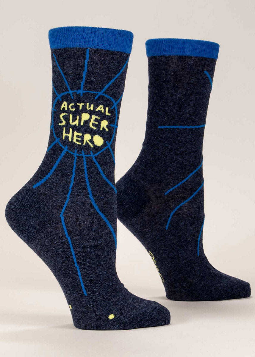 Navy women&#39;s crew socks that say “Actual Super Hero&quot; in yellow on the leg with abstract doodle embellishments in blue.