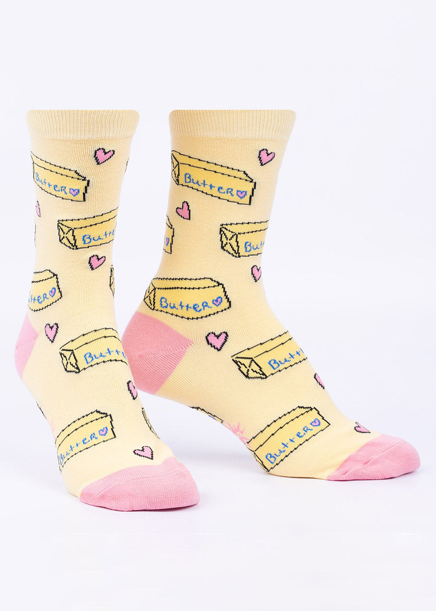 Women's crew socks in pale yellow with an allover pattern of sticks of butter with doodle-style pink hearts in between.