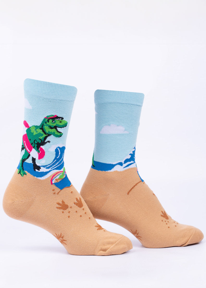 Blue and tan women&#39;s crew socks  show a T. rex at the beach complete with sun visor, a pail for building sandcastles and an inner tube float.