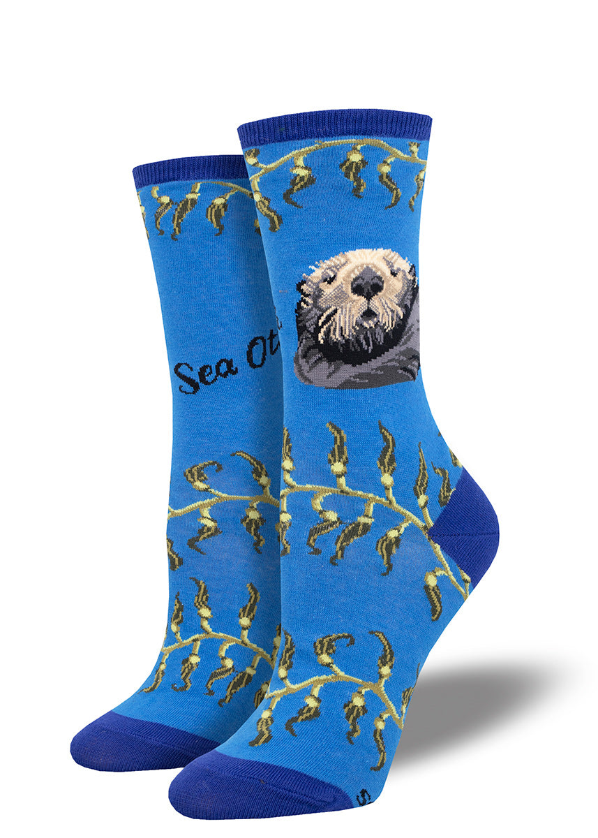 Blue women&#39;s crew socks with the portrait of a sea otter and stripes of green kelp.