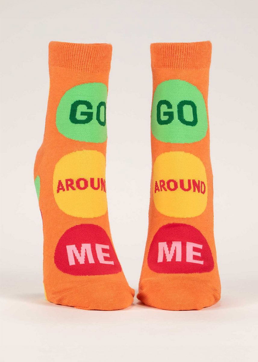 Bright orange women&#39;s ankle socks say “Go Around Me” inside of green, yellow and red circles reminiscent of a traffic signal. 