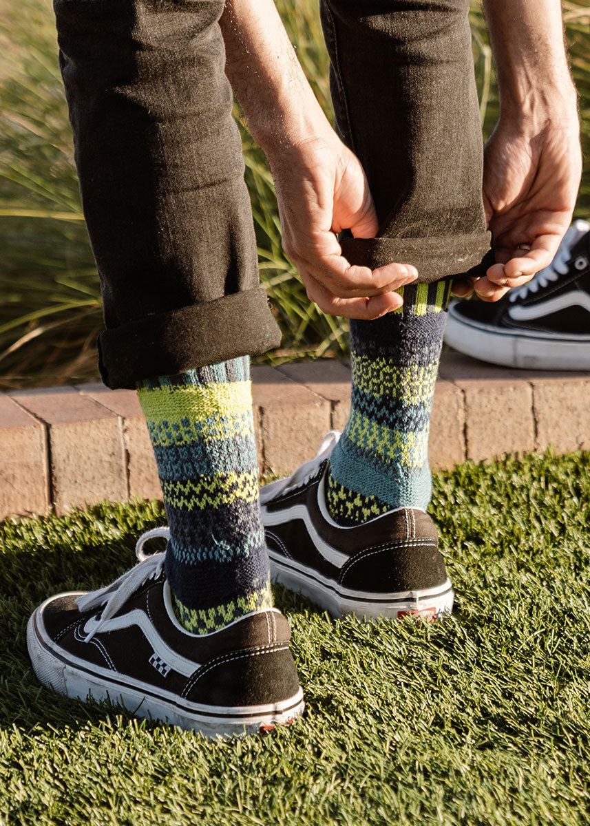 Intentionally mismatched crew socks with different sections featuring various geometric patterns like stripes and dots in shades of blue, lime green and dark gray.