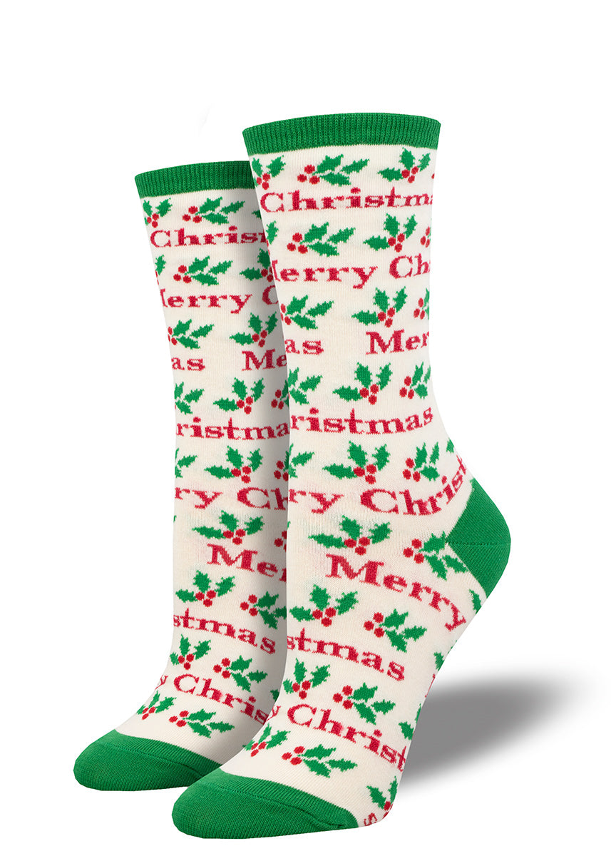 White novelty holiday socks for women with a dark green cuff, toe, and heel featuring an allover pattern of holly leaves and the words "Merry Christmas" in a red font.