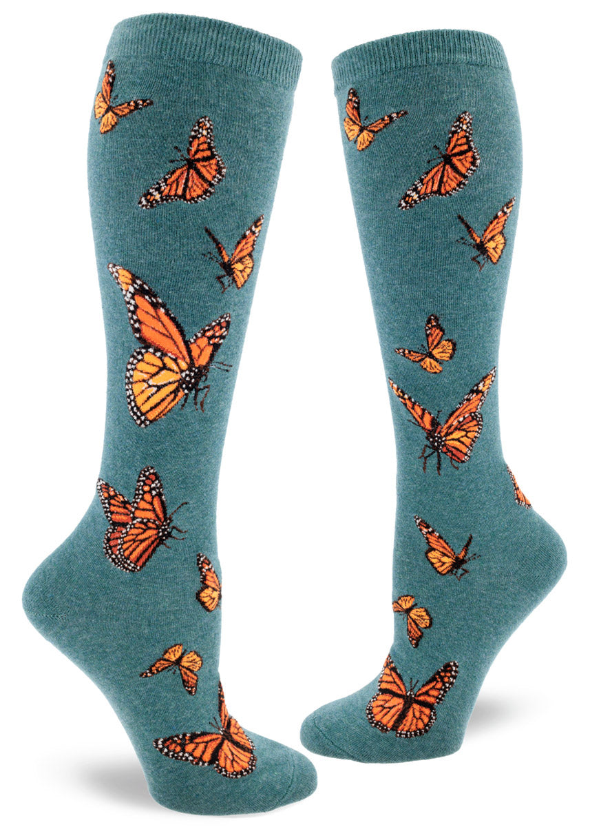 Dark teal knee socks for women with an allover pattern of orange monarch butterflies in various poses in flight.