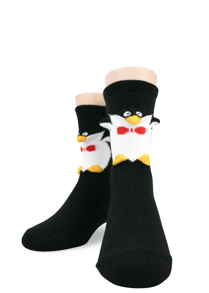 Black and white crew socks with a 3D knitted penguin face, flippers, and yellow feet to make kids' feet look like penguins wearing red bowties. 