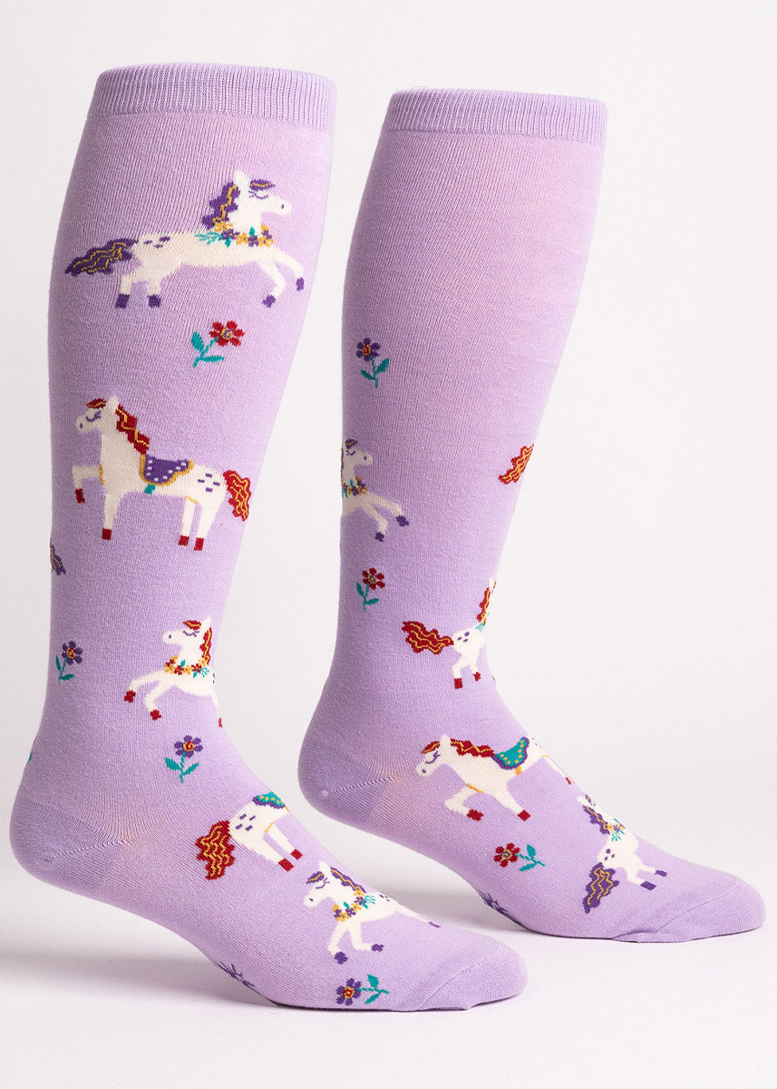 Lavender knee socks designed for wide calves with an allover pattern of white horses with colorful manes and accessories like floral necklaces and saddles, as well as flowers. 