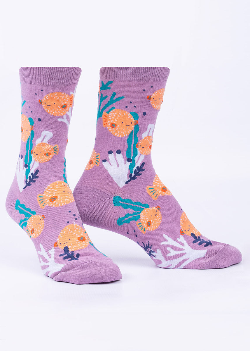 Women&#39;s crew socks with orange pufferfish swimming between seaweed and corals on a light purple background.