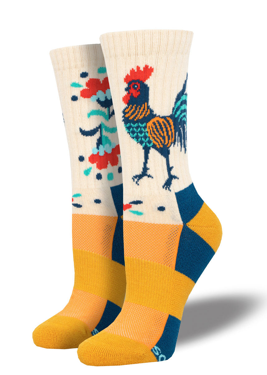 White, yellow, and dark blue striped hiking socks for women that depict a red, yellow, and light blue rooster design on one side and a floral design on the other.