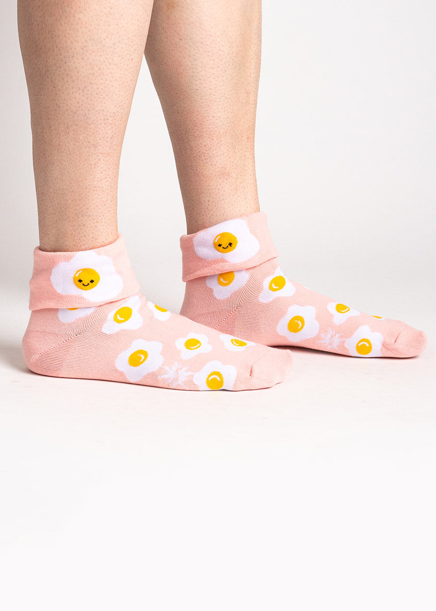 A model poses wearing light peach turn-cuff crew socks for women with an allover pattern of fried eggs. 