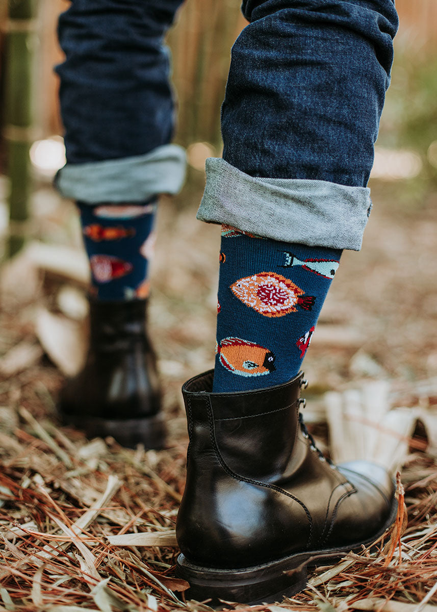A model wearing tropical fish-themed novelty socks poses walking outside in a bamboo forest.