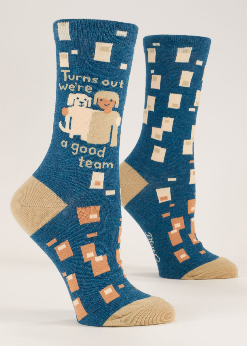 Dark blue crew socks for women that say "Turns out we're a good team" on them and have a design of a labrador dog and their owner with their arms around each other against a geometric pattern of squares.