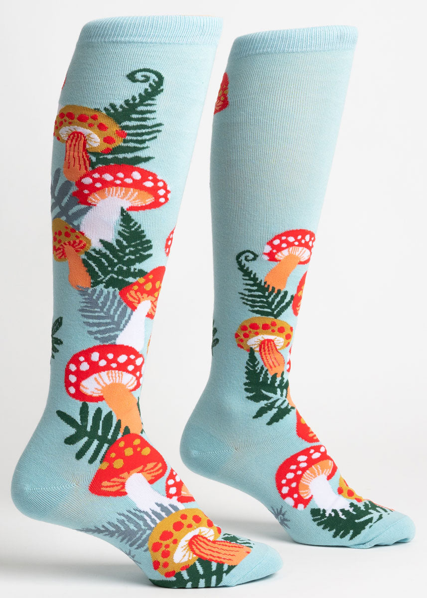 Light blue knee socks for women with colorful red, orange, and yellow toadstool mushrooms growing up the leg along with green foliage.