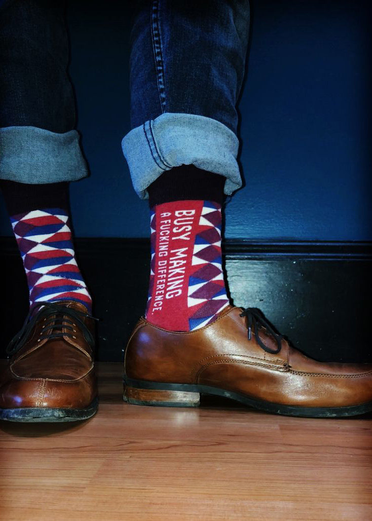 Swear word socks for men feature geometric patterns and the words, &quot;Busy making a fucking difference.&quot;