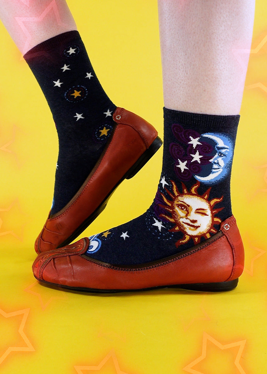 Celestial crew socks for women feature a grinning blue moon and a winking yellow sun on a heather blue background.