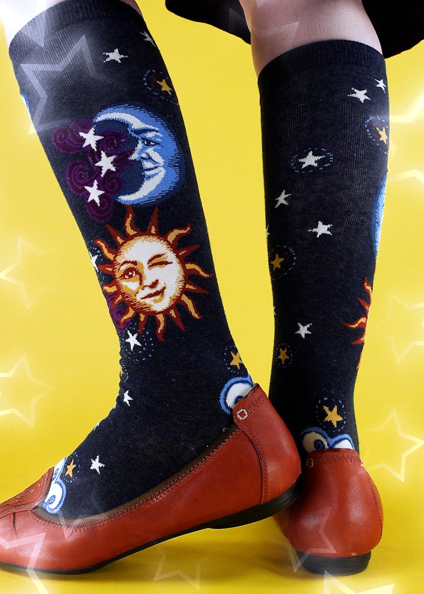 Celestial knee-high socks feature a stylized sun, moon, and stars on a heather blue background.