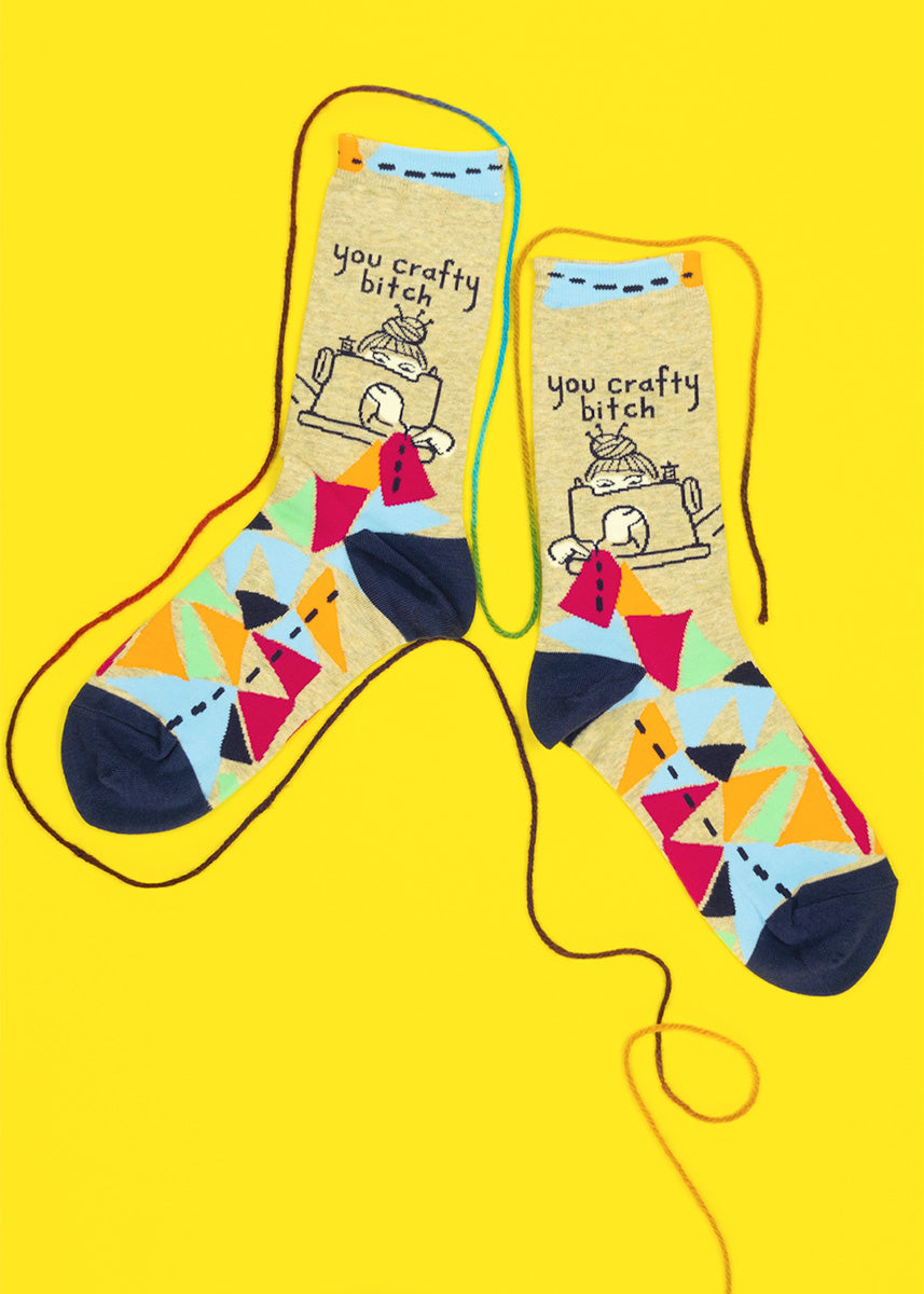 Funny craft socks for women show a woman stitching scraps at her sewing machine with the words, &quot;You Crafty Bitch.&quot;
