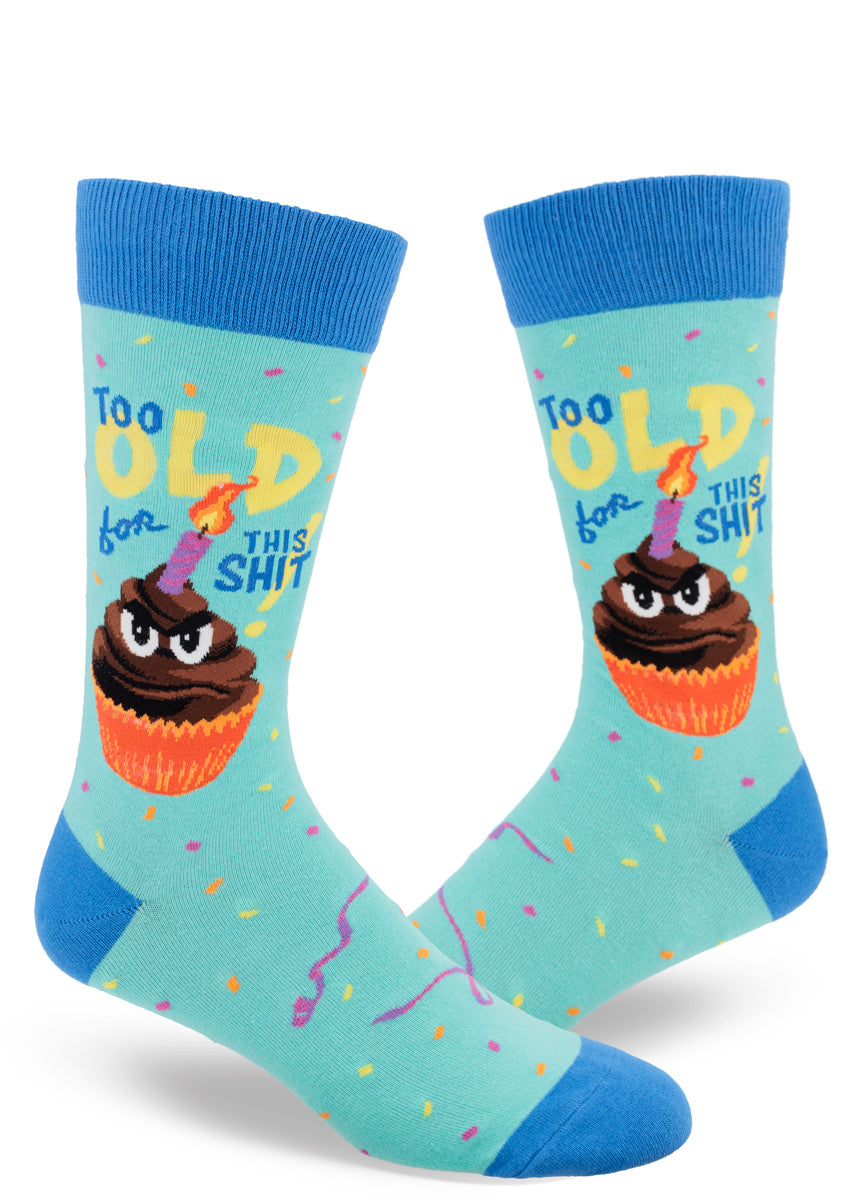 Birthday crew socks for men feature a grumpy anthropomorphized cupcake with a candle stuck in his chocolate frosting and the words “Too Old for This Shit!”