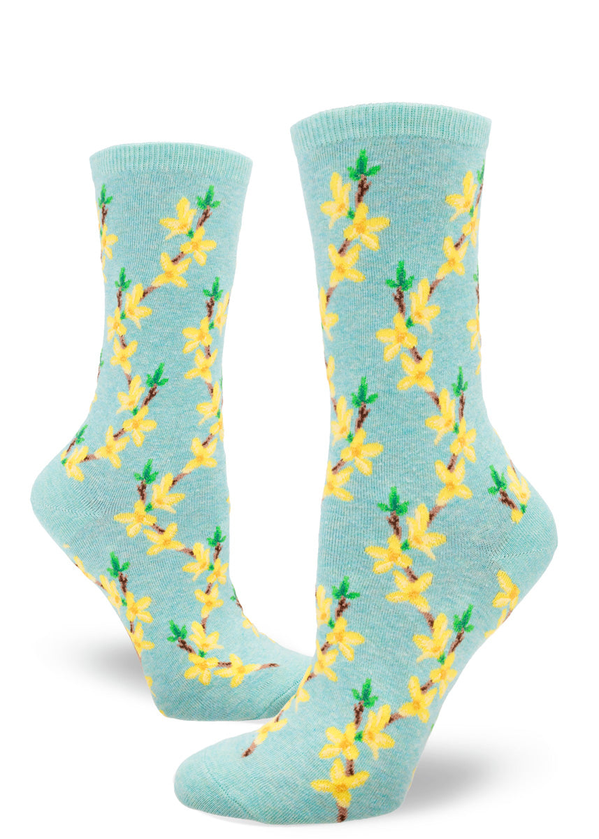 Floral women&#39;s crew socks feature a repeating pattern of forsythia flowers, the yellow buds arranged along brown branches, over a pale aqua heather background.