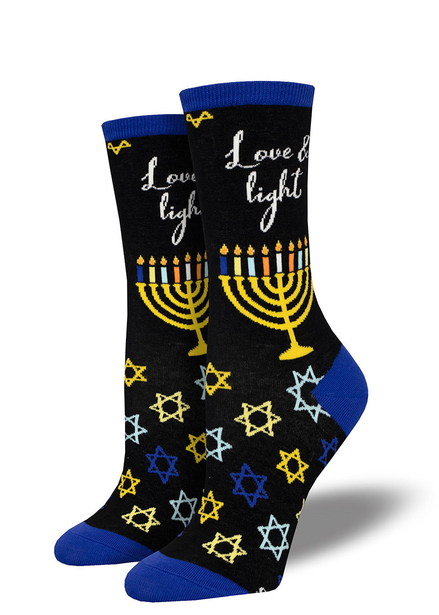 Black crew socks with a Hanukkah design featuring a lit menorah and the words “Love &amp; Light,” with a scattering of stars of David across the foot.