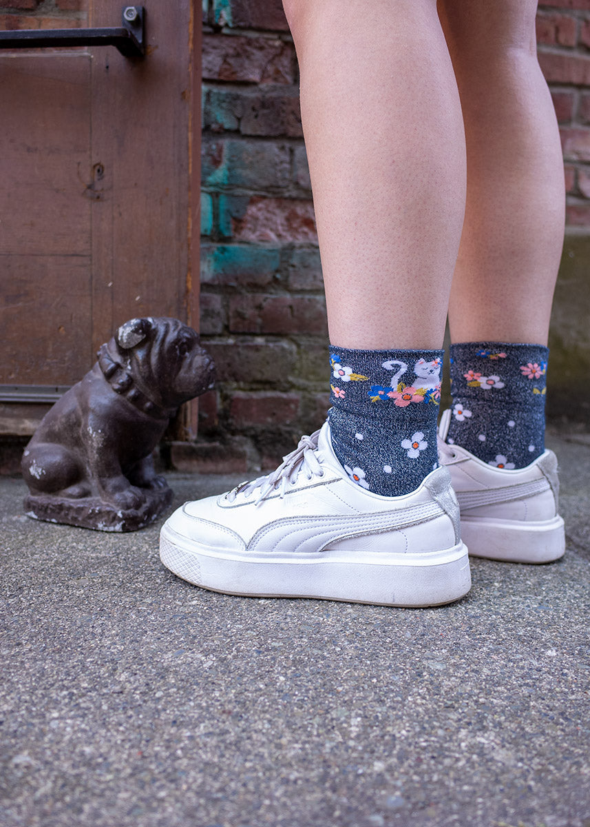 A model wearing sparkly cat novelty socks and white sneakers poses outside by a small bulldog statue