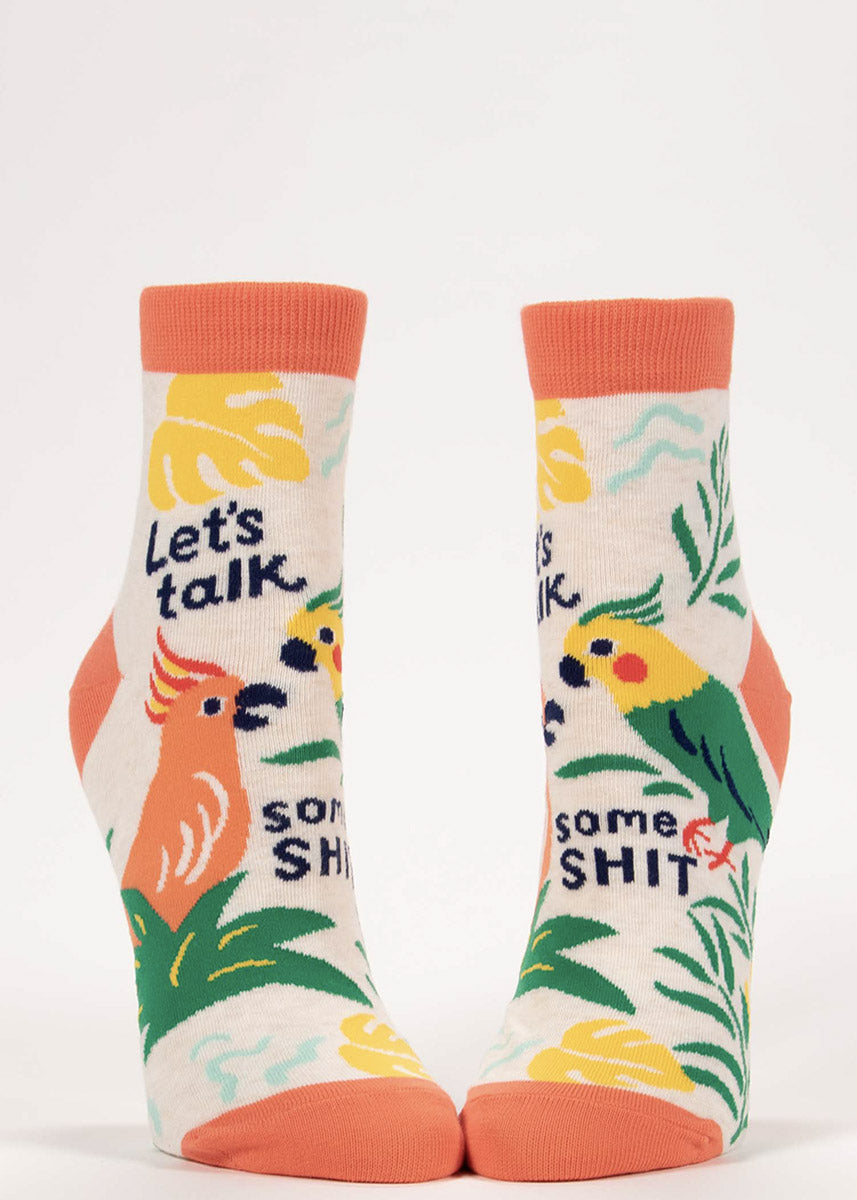 Cream-colored ankle socks with orange accents feature colorful parrots and tropical plants with the words “Let's Talk Some Shit.” 