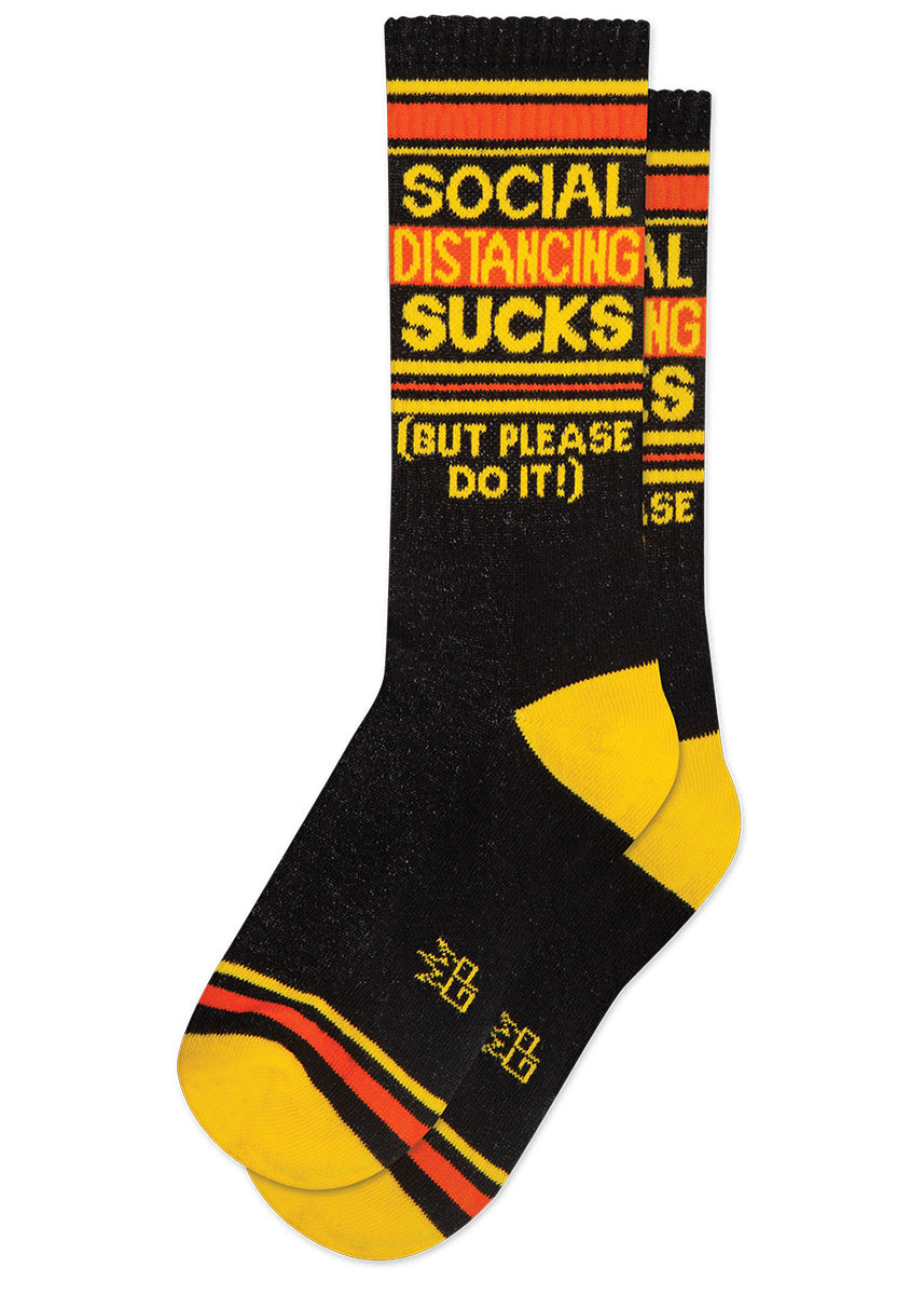 Funny gym socks say "Social Distancing Sucks (But Please Do It!)" with bright yellow and orange stripes on a black background.
