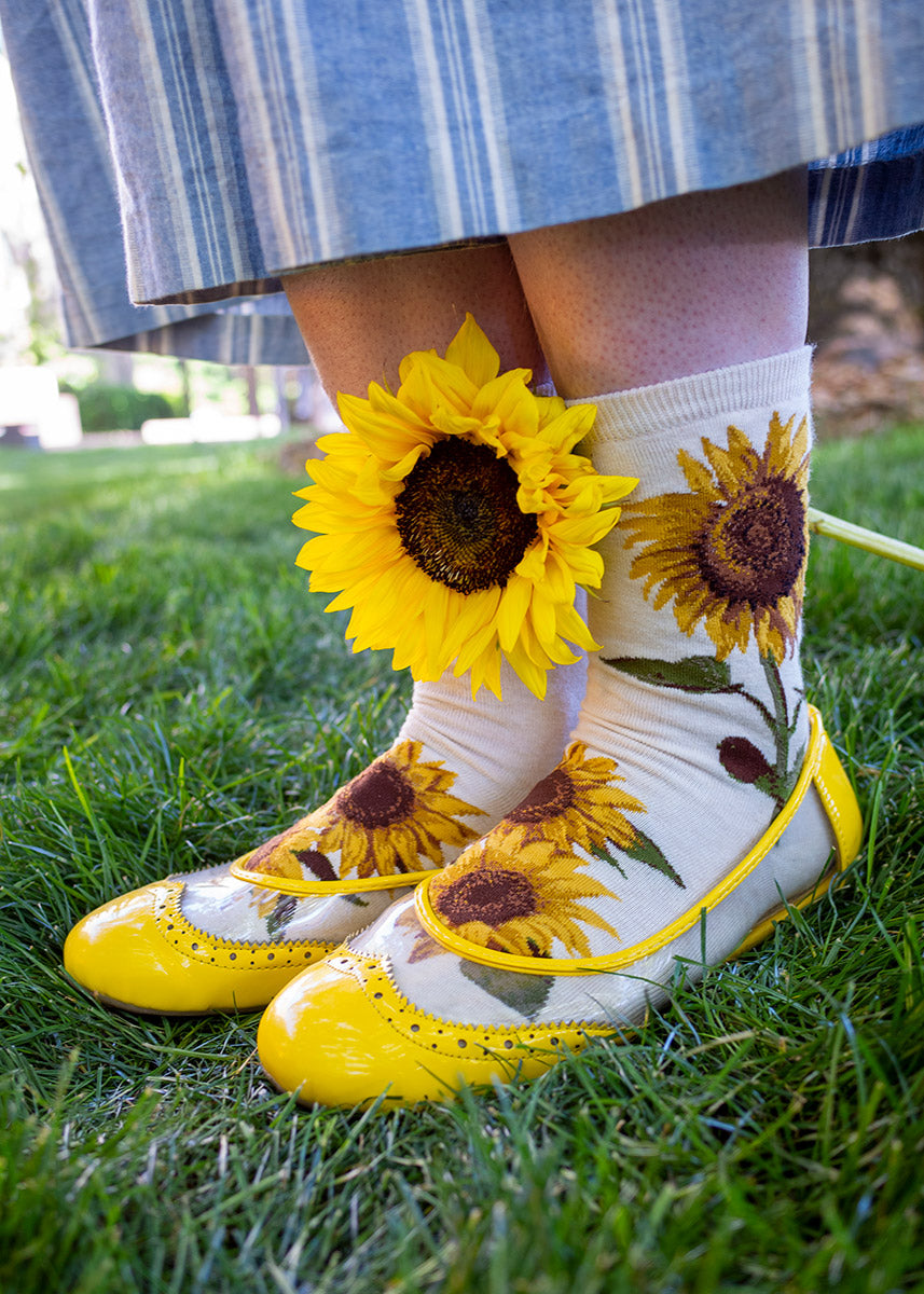 A woman wears floral socks with golden yellow sunflowers on a cream background.