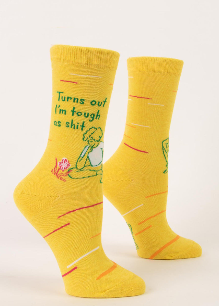 Funny crew socks for women show a person looking at a blooming flower with the words, "Turns out I'm tough as shit," on a bright yellow background.