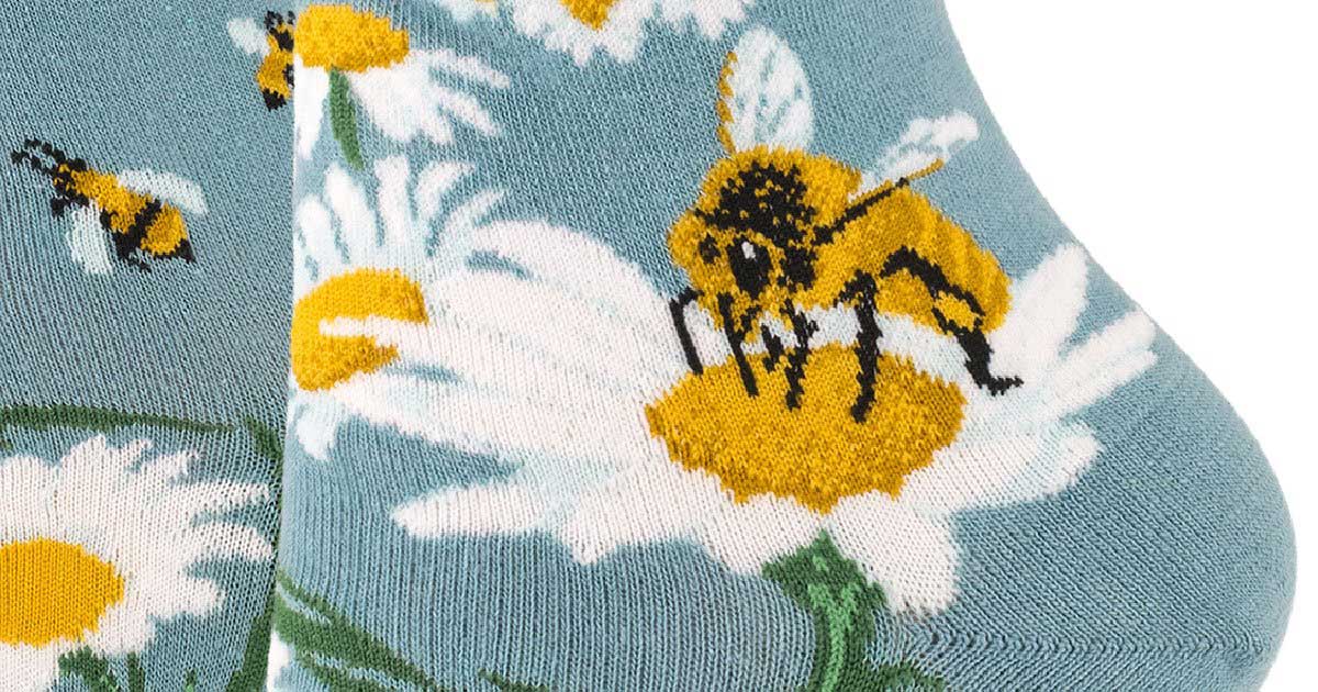 Give Bees a Chance Socks by ModSocks are slate blue crew socks covered in a design of bees and daisies, the flowers forming a big peace sign above the ankle.