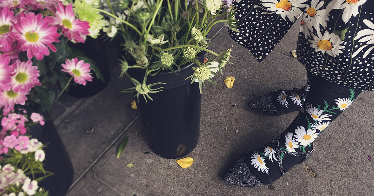 Daisy flower socks with white flowers on a black background, next to florist's blooms.