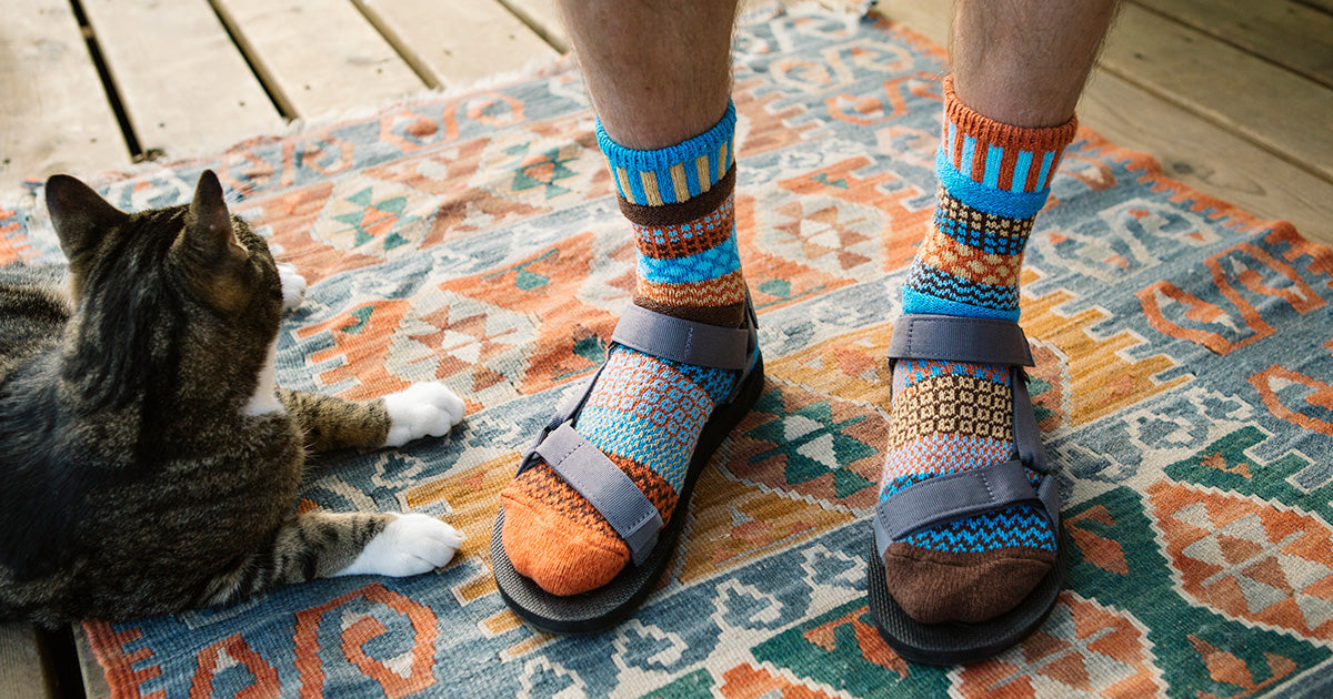 Extra large men's socks in a colorful mismatched pattern of blue and orange, worn with sandals.