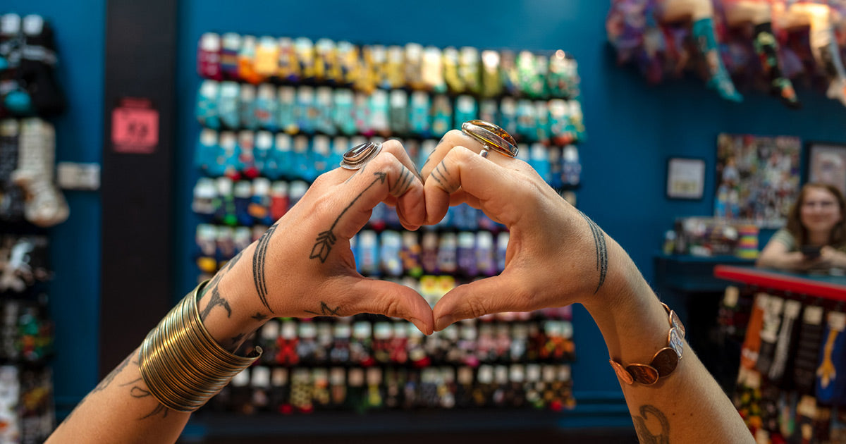 An employee makes a heart gesture with her hands in front of a wall of colorful socks at Cute But Crazy sock shop in Bellingham, Washington.