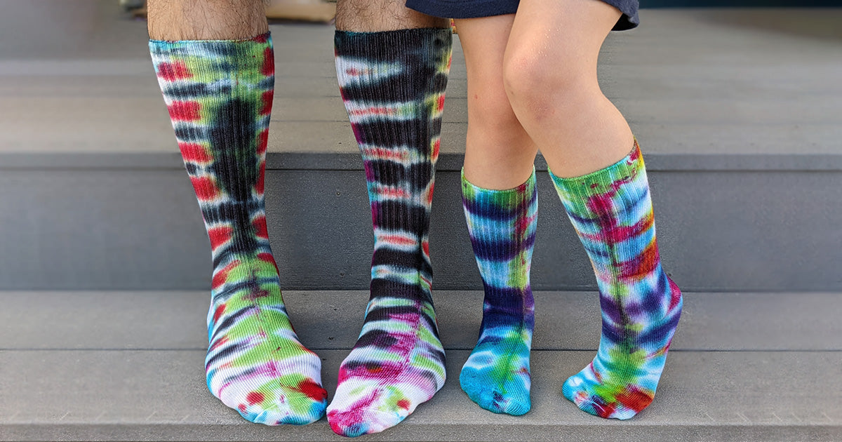 A man and a child wear tie-dye socks made at Cute But Crazy Socks