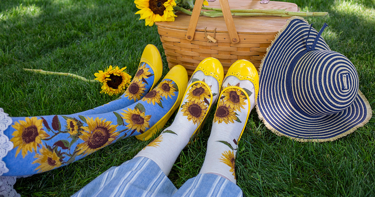 Two people sit next to each other on grass wearing short and long versions of the same sunflower socks in white and blue