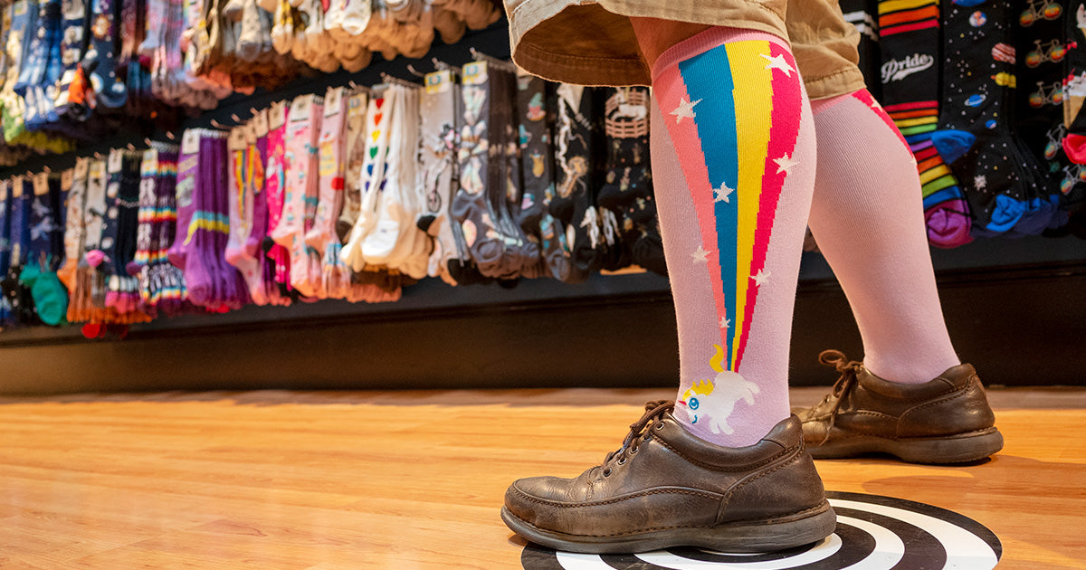 Rainbow unicorn knee socks are worn by a man next to a display of socks Cute But Crazy Socks in Bellingham, Washington.