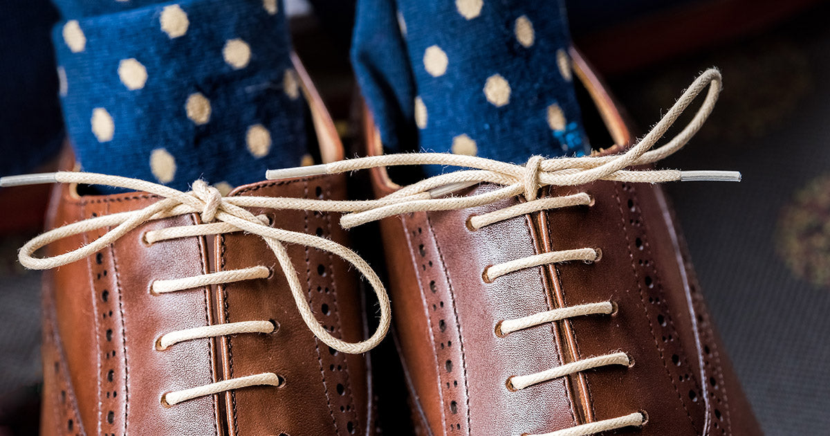 Navy blue men's dress socks with polka dots, displayed with brown leather shoes.