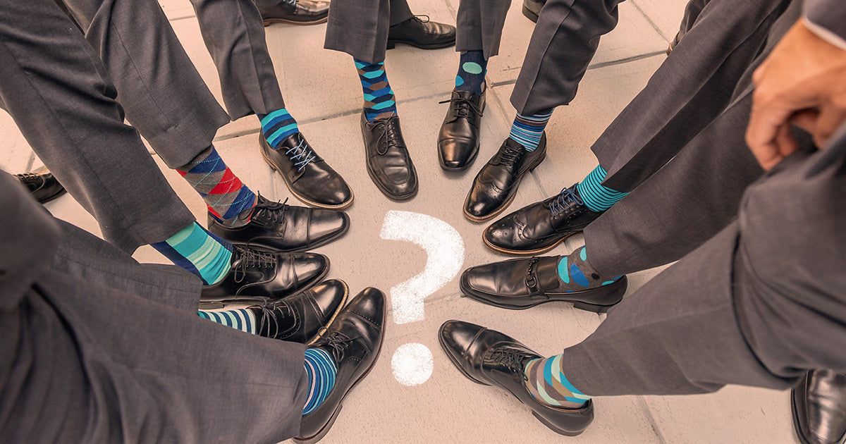 Groomsmen wear matching gray suits and black shoes, each showing off a unique pair of novelty socks.