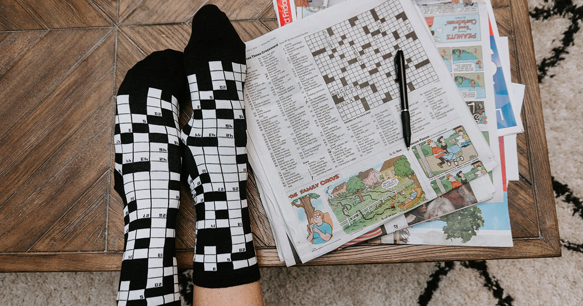 Crossword socks are a fun twist on the checkerboard fashion trend, shown here next to a newspaper crossword puzzle.