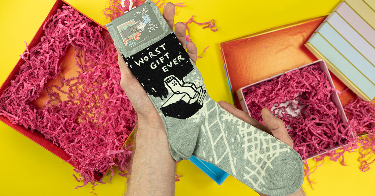 A man receives a pair of funny socks that say "Worst gift ever" on the side, as a gift for a special occasion.