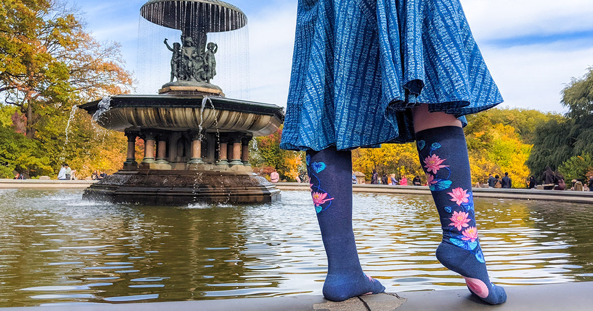 Lotus knee socks worn with matching blue skirt posed on the edge of a fountain.