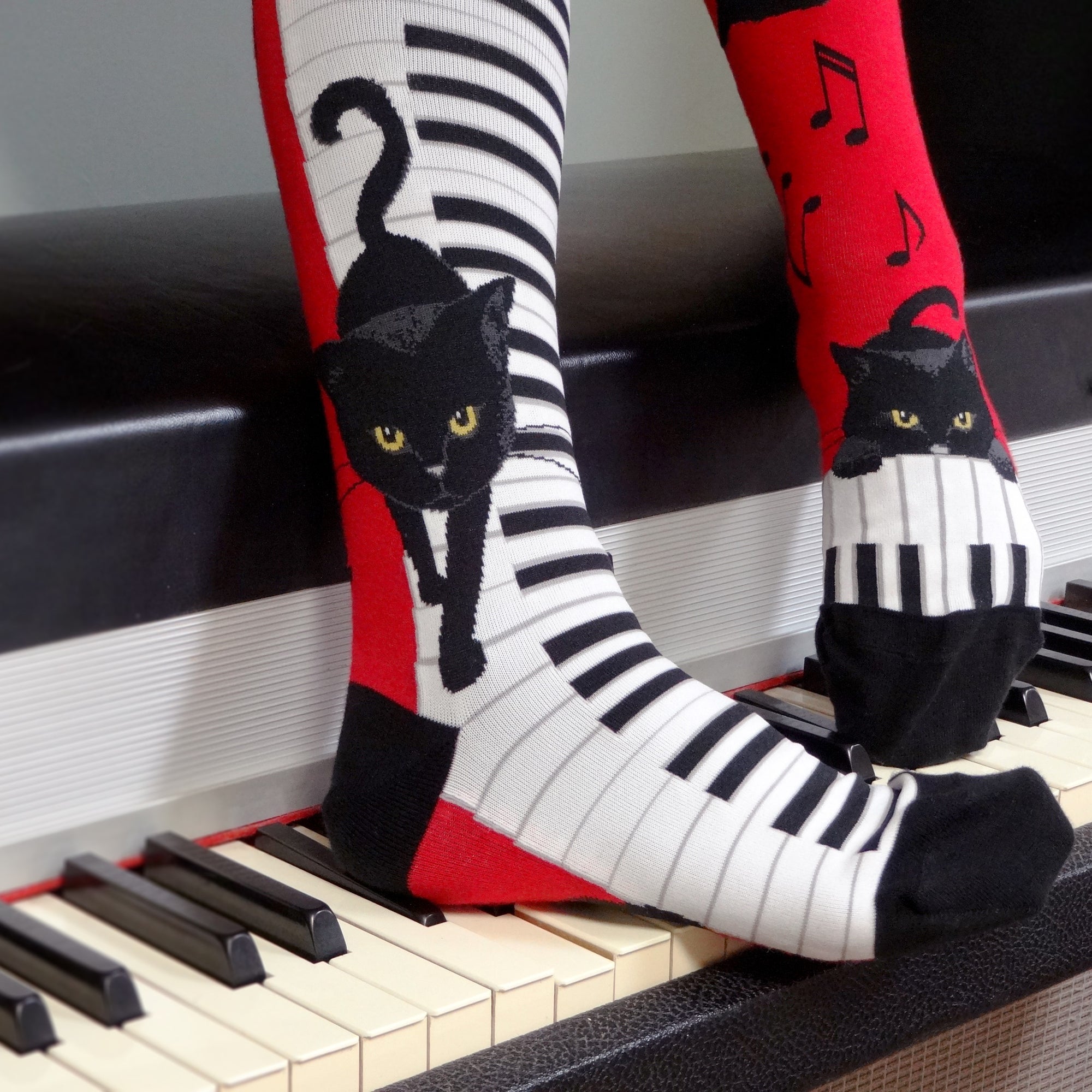 On these red knee highs with a black heel and toe are cute black cats with orange eyes prancing and playing on white and black piano keys with black music notes floating around them. In our Cat Socks collection you can find tons of cute cat socks! 