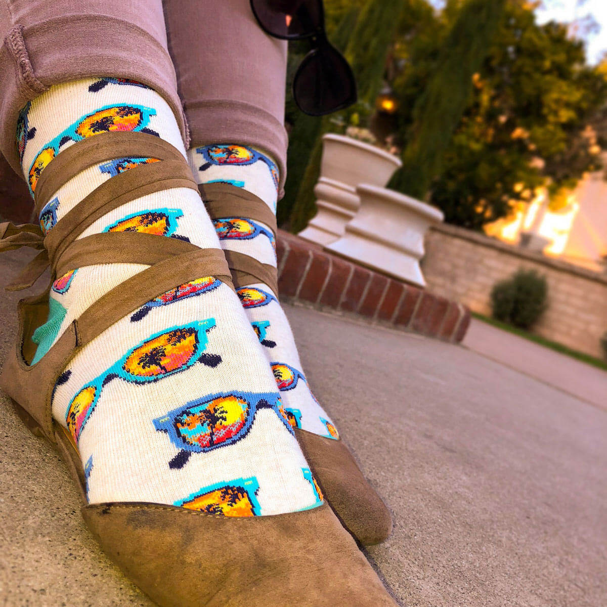 These ivory crew socks feature cute blue summer sunglasses reflecting a colorful sunset and palm trees.