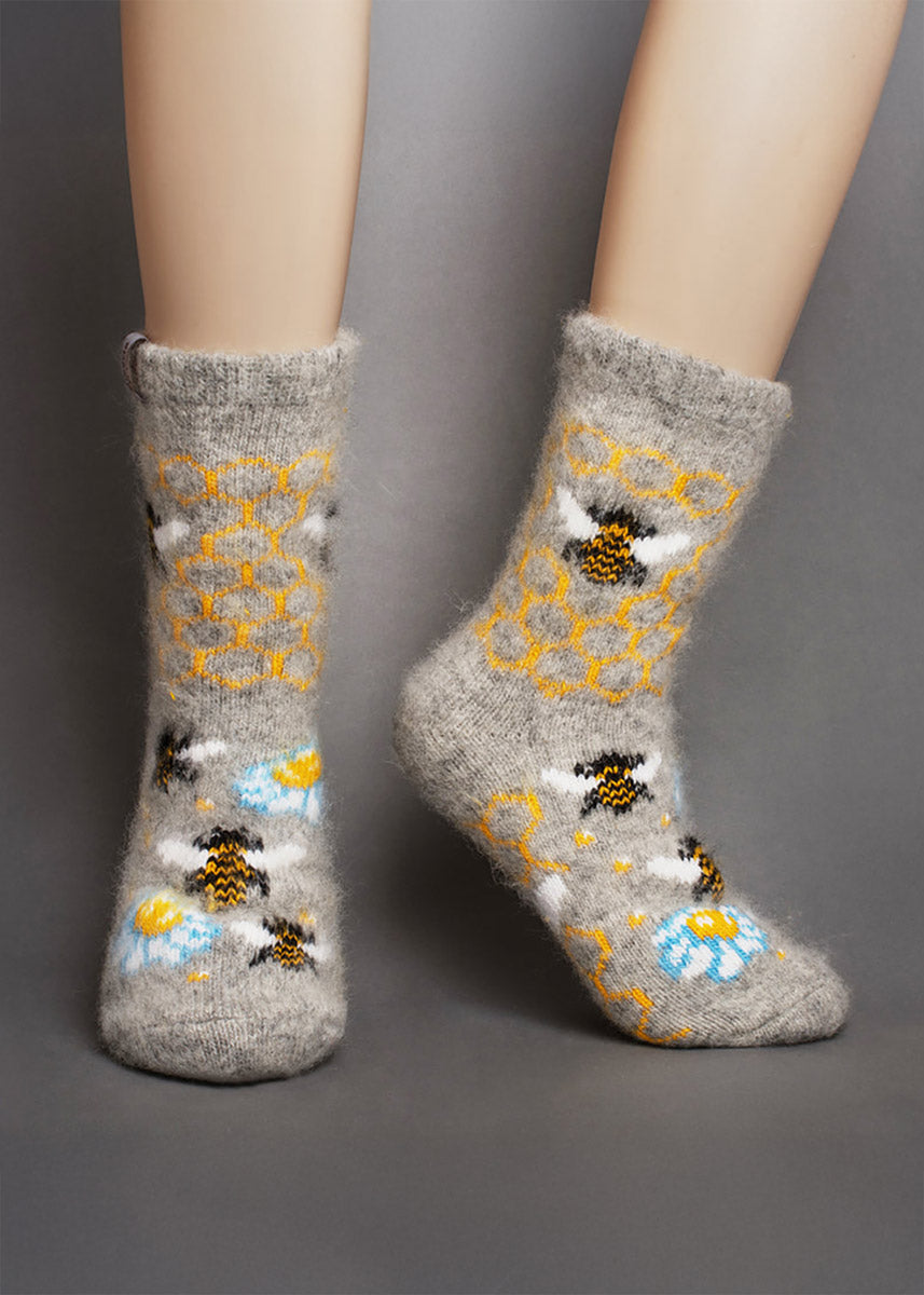 Gray fuzzy socks with bee and flower patterns displayed on legs in front of a gray background.