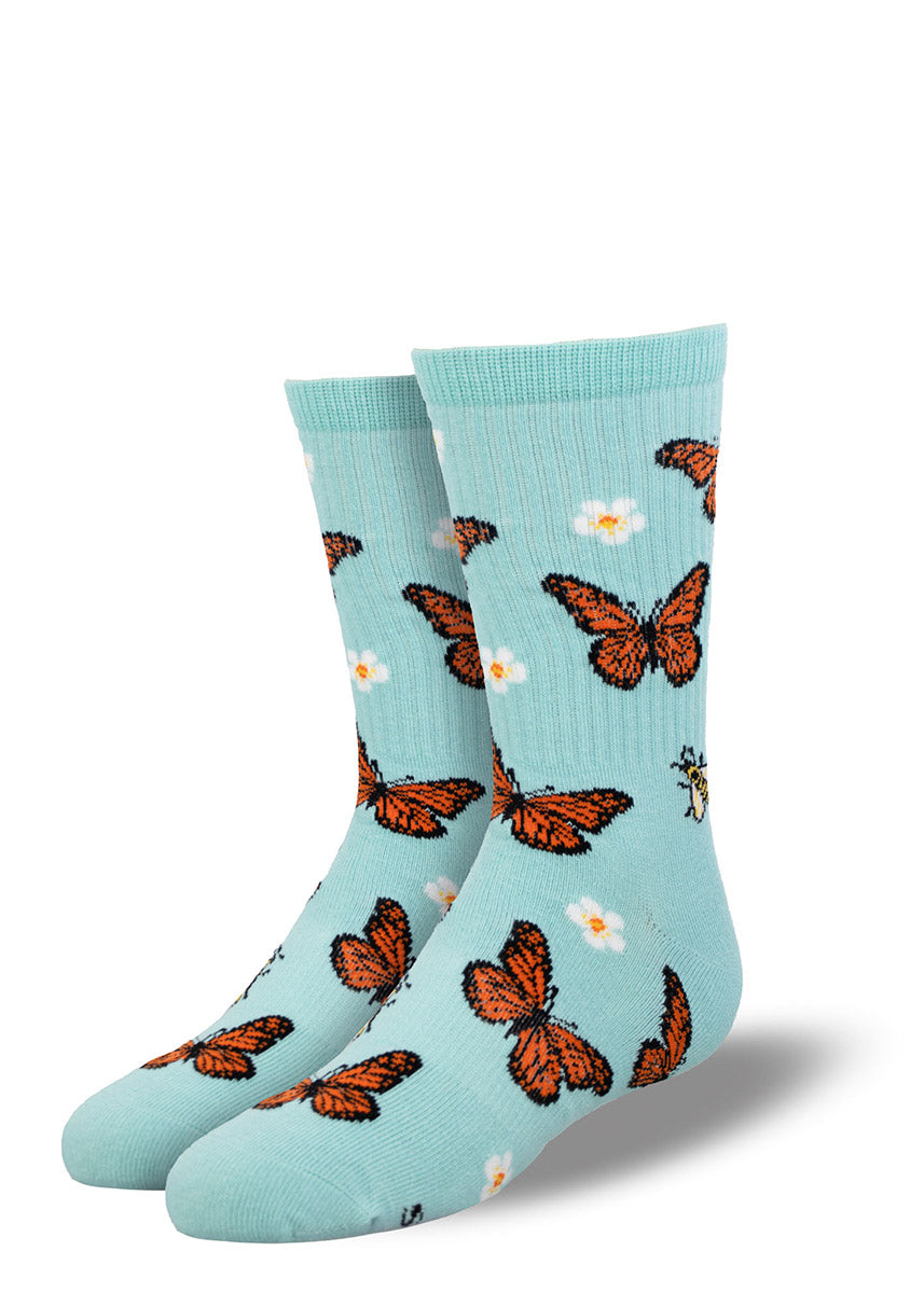 Sky blue athletic crew socks for kids with an allover pattern of orange monarch butterflies, yellow bumblebees, and white flowers. 