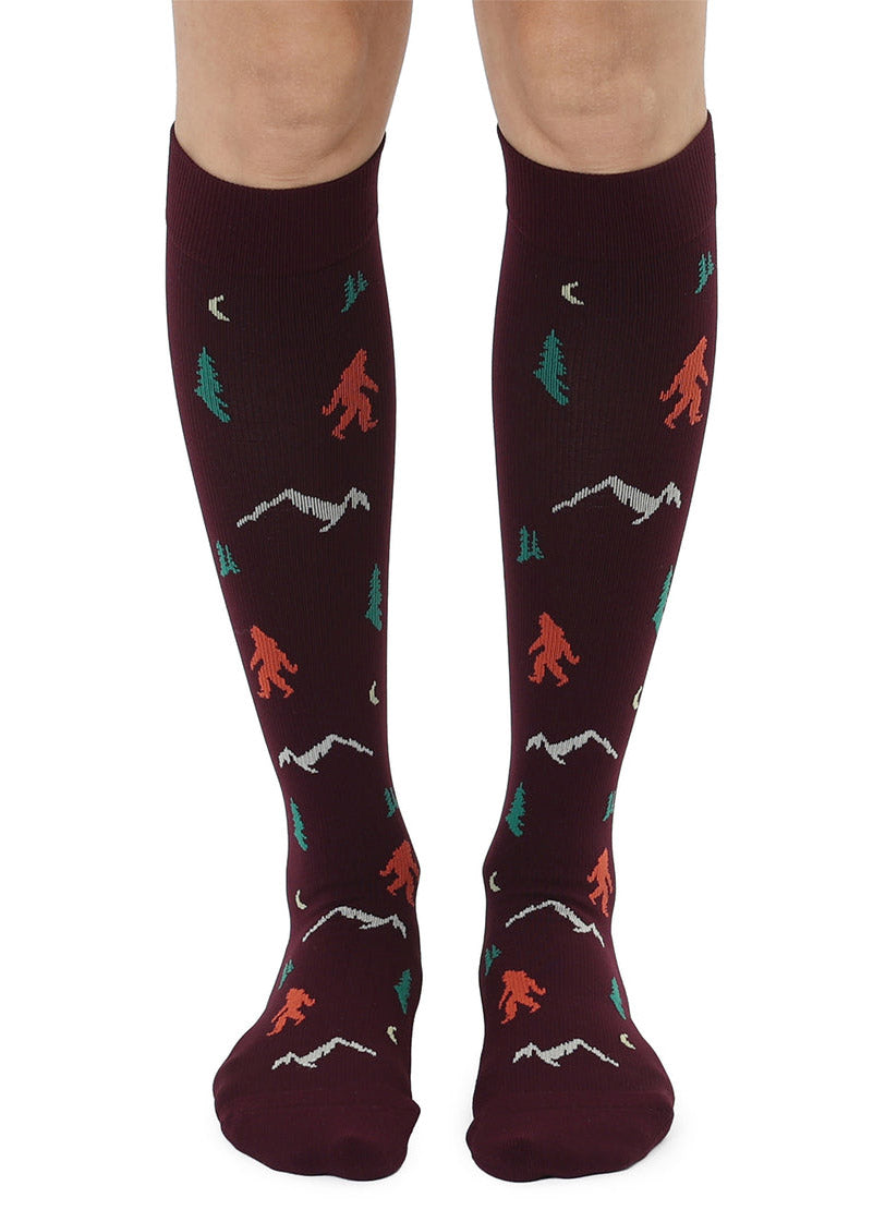 Knee-high brown compression socks with a repeating Sasquatch and mountain pattern.