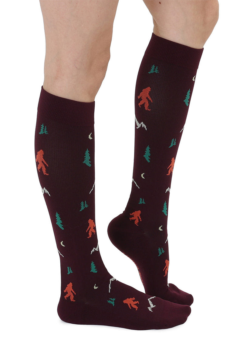 Knee-high brown compression socks with a repeating Sasquatch and mountain pattern.