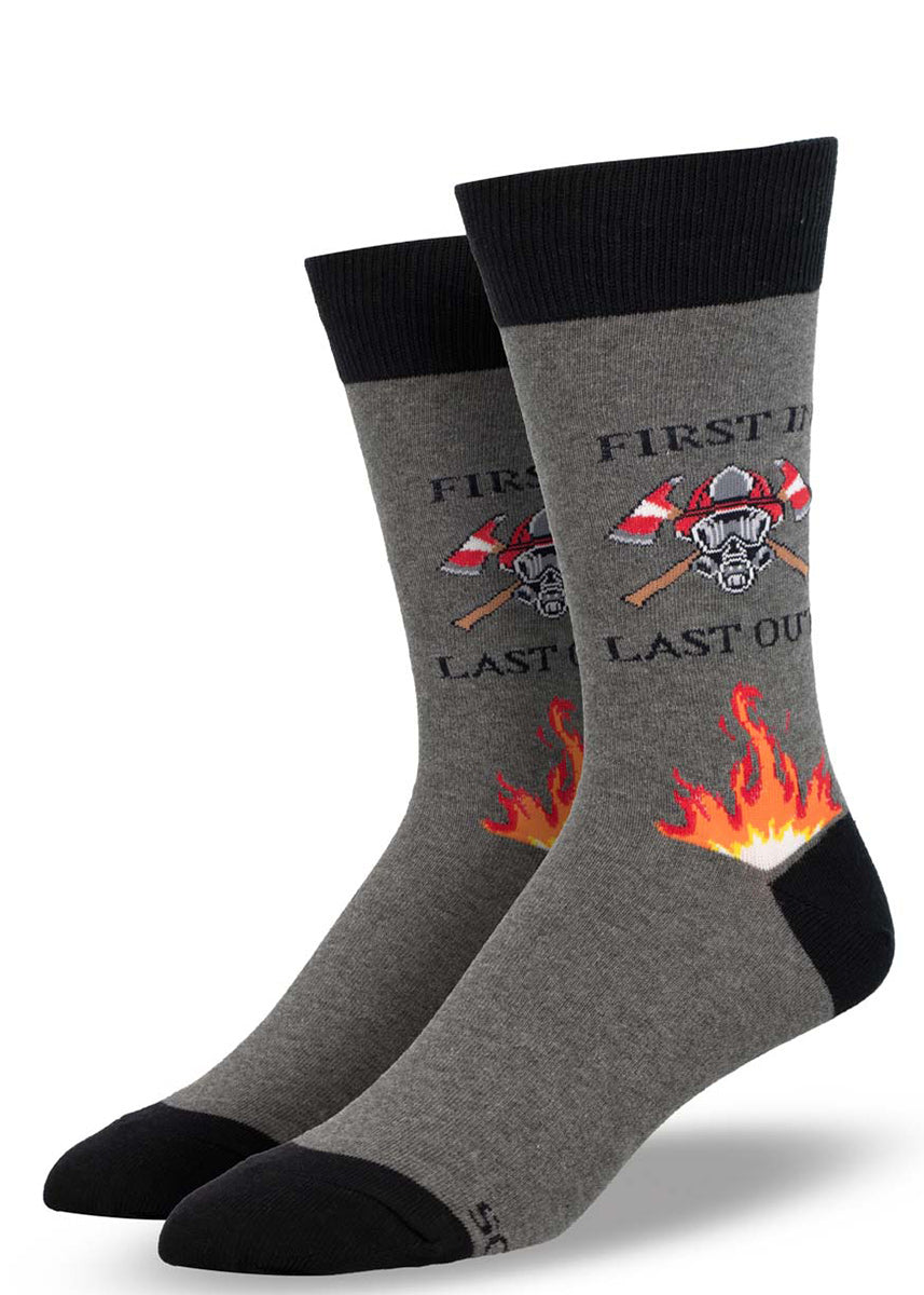 Dark gray crew socks for men with a design featuring a firefighter mask, axes, orange flames, and the words "First In, Last Out." 