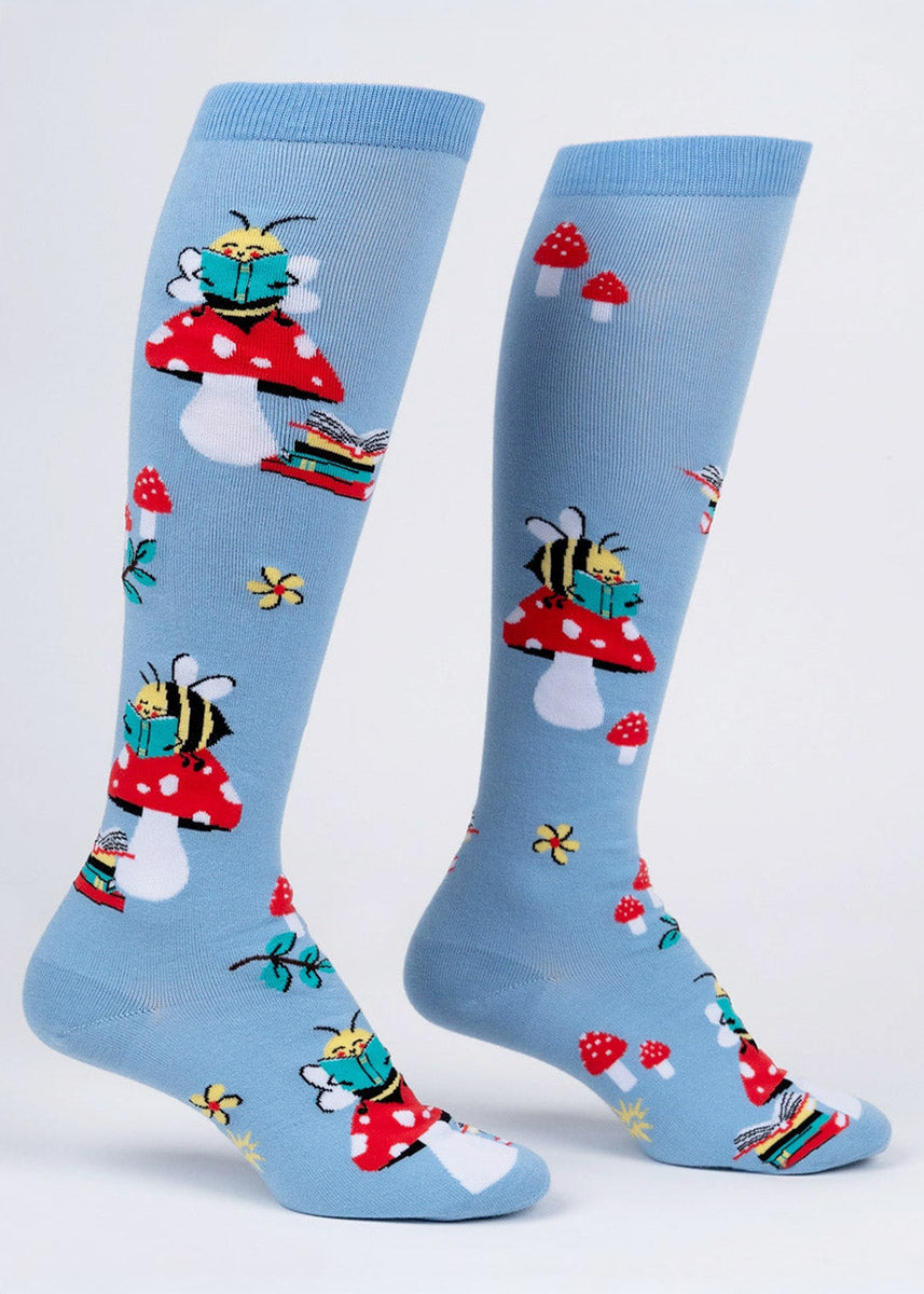 Light blue knee socks for women with a pattern of bumblebees reading a book atop toadstool mushrooms.